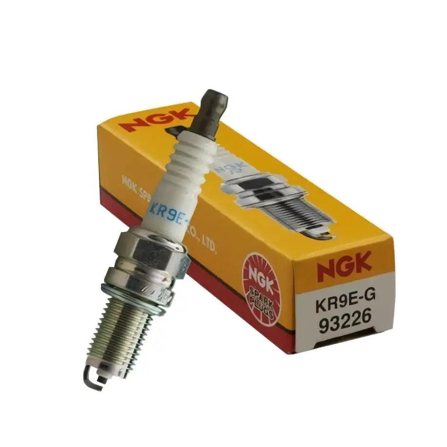 Ngk kr9e-g tennplugg med sølvfarget metallkropp og hvit keramisk isolator ved siden av gul og rød emballasje